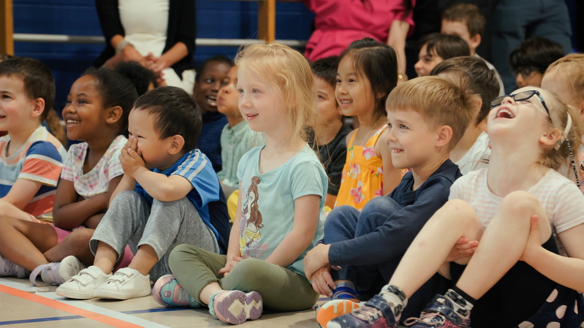 Close-up of children sitting down at an assembly inside a gym.