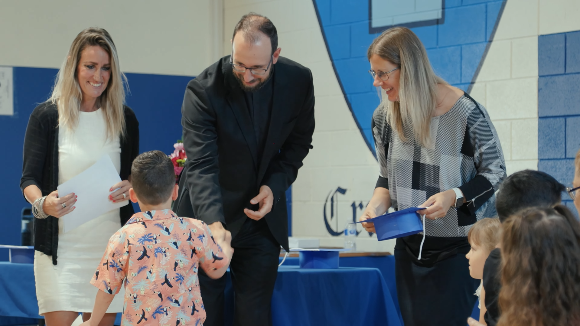 Teacher and pastor at kindergarten grad, giving a child his certification.